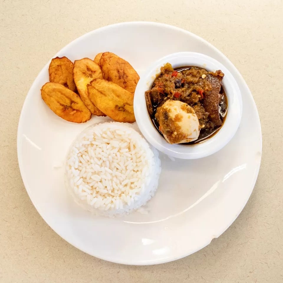 A plate of white rice, fried plantains, and a stew with meat and a hard-boiled egg.