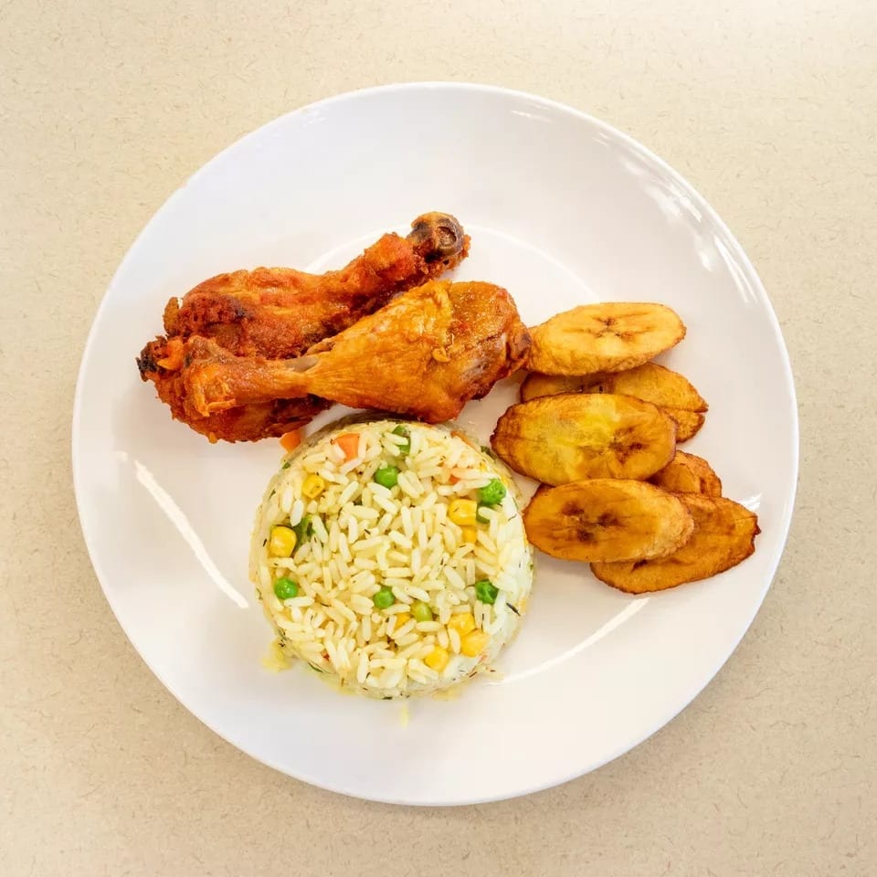 Fried chicken drumsticks, vegetable rice, and plantain slices on a white plate.